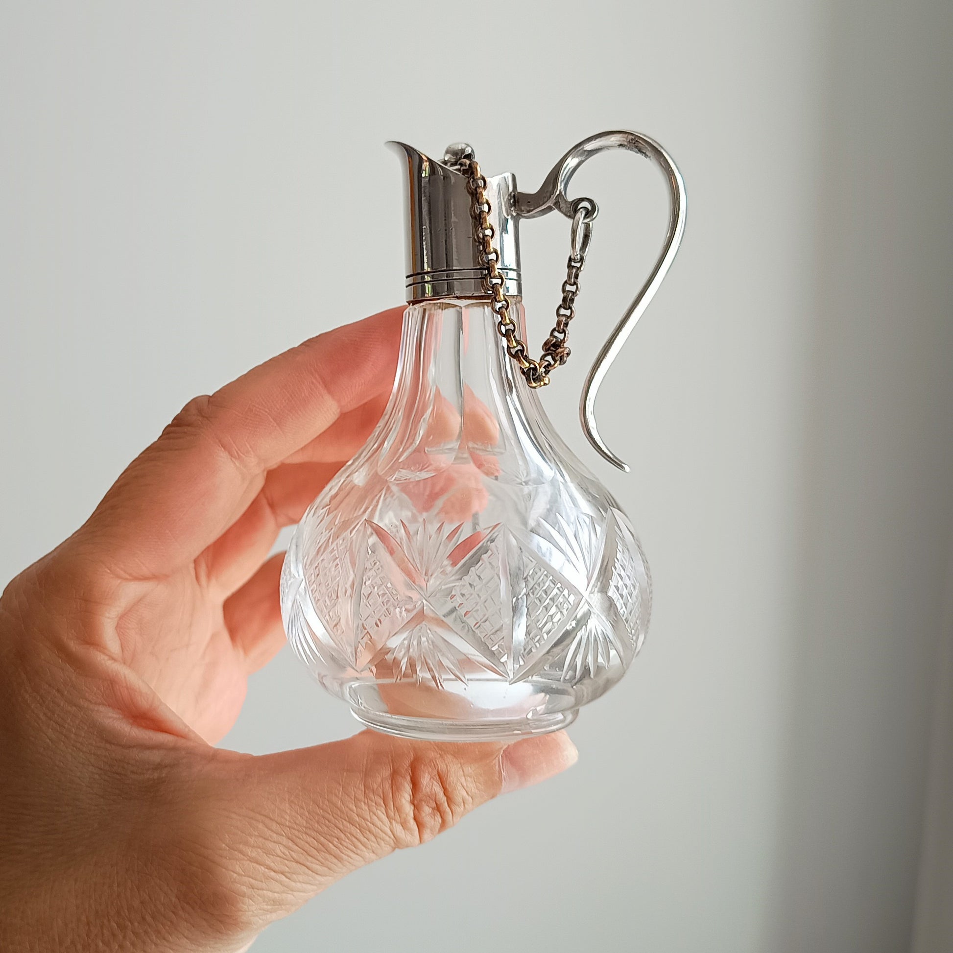 decorative glass bottle with a silver top handle and chained stopper