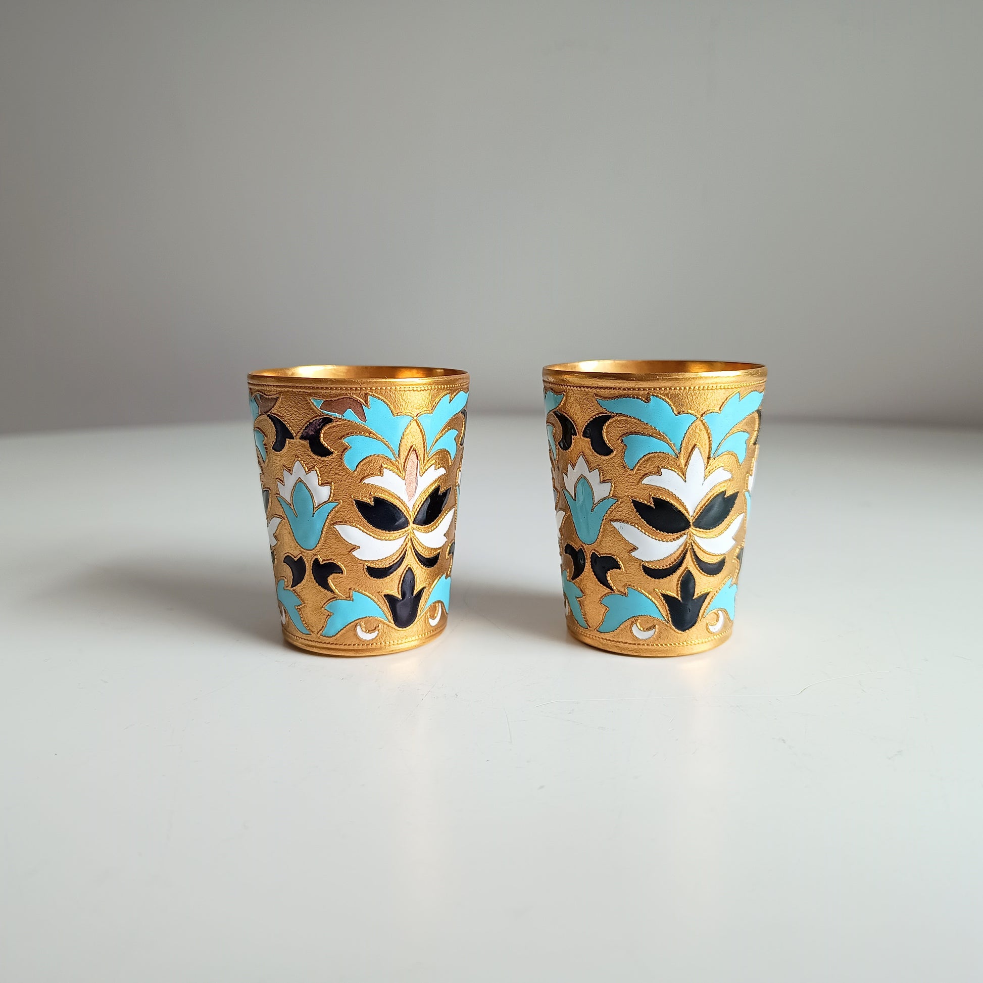 Two ornate Russian enamelled blue white and gold shot glasses with floral designs