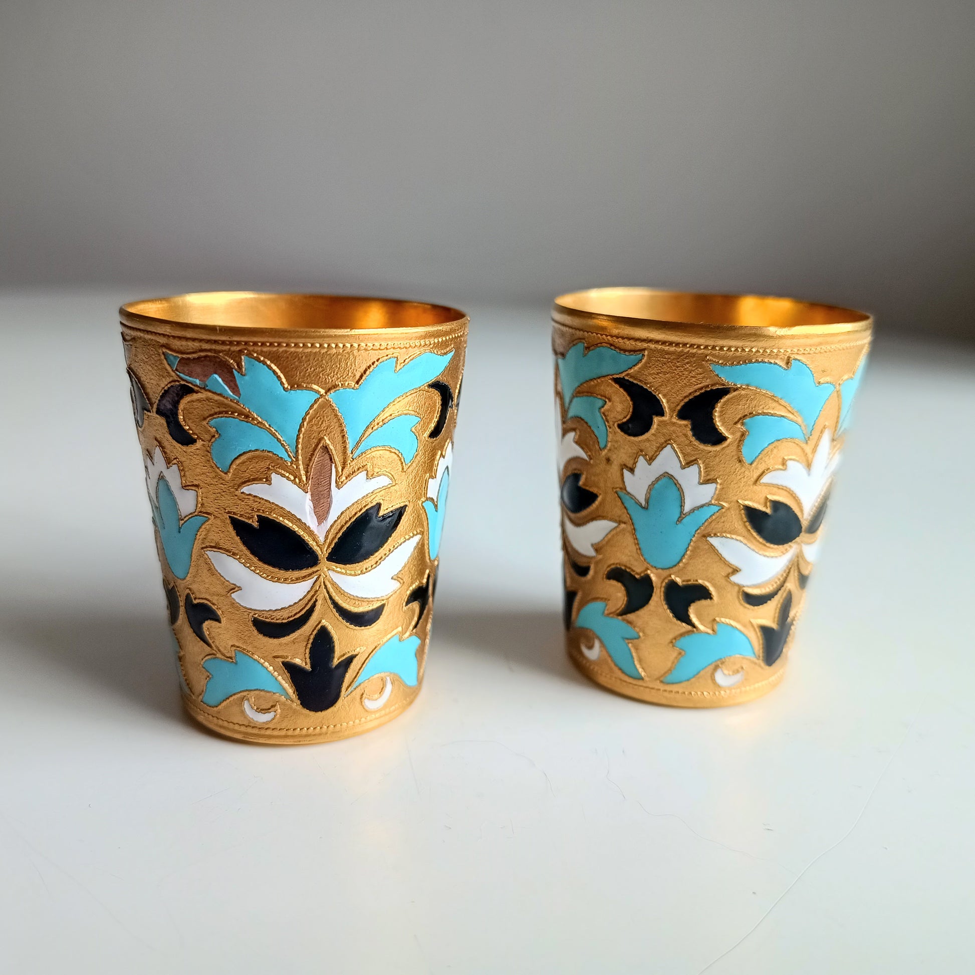 Two ornate Russian enamelled blue white and gold shot glasses with floral designs