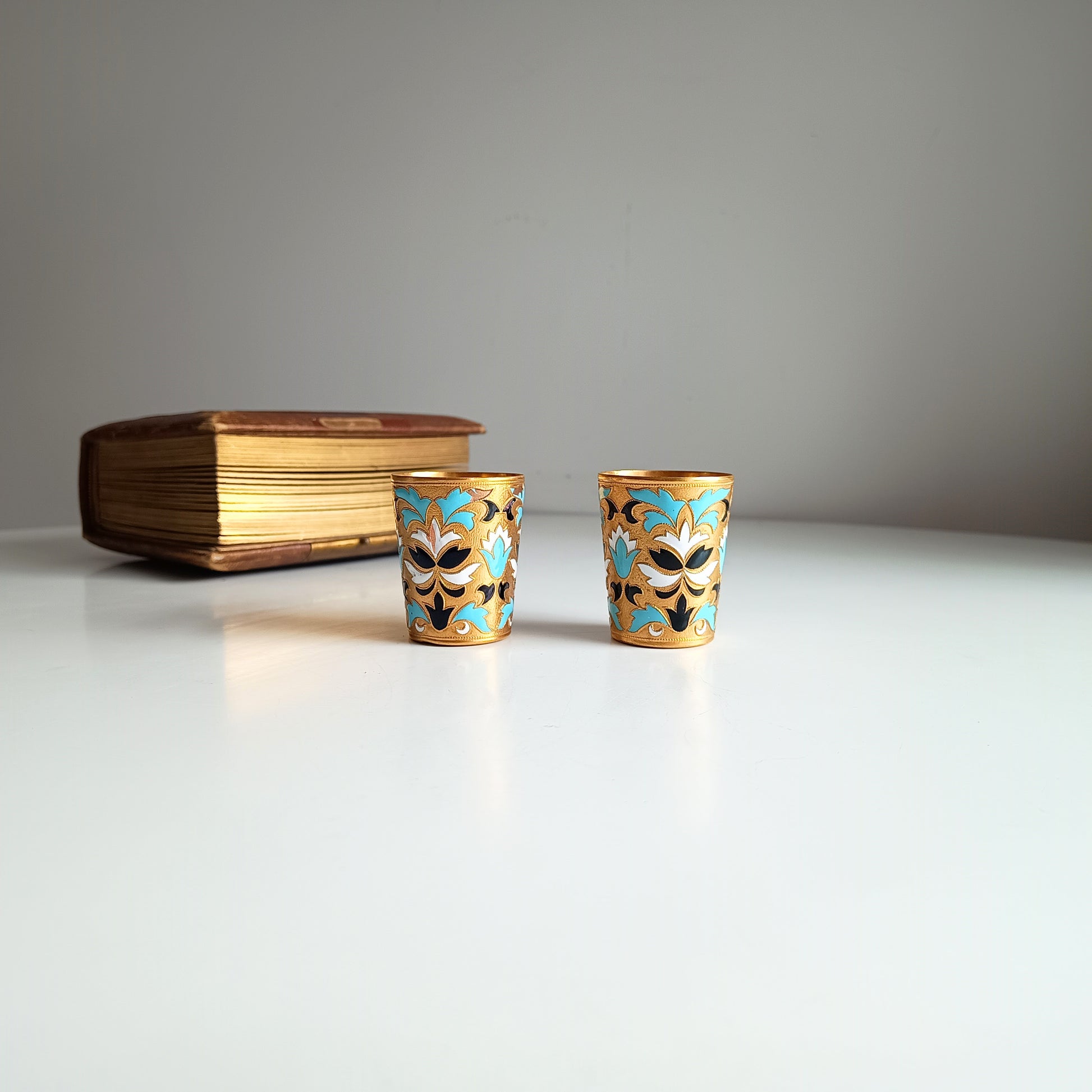 Two ornate Russian enamelled blue white and gold shot glasses with floral designs