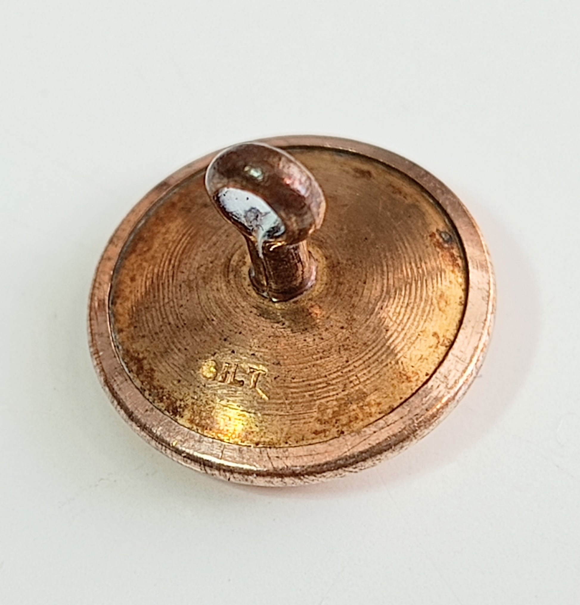 Close-up of an antique bronze or copper-colored object button with 'gilt' stamp