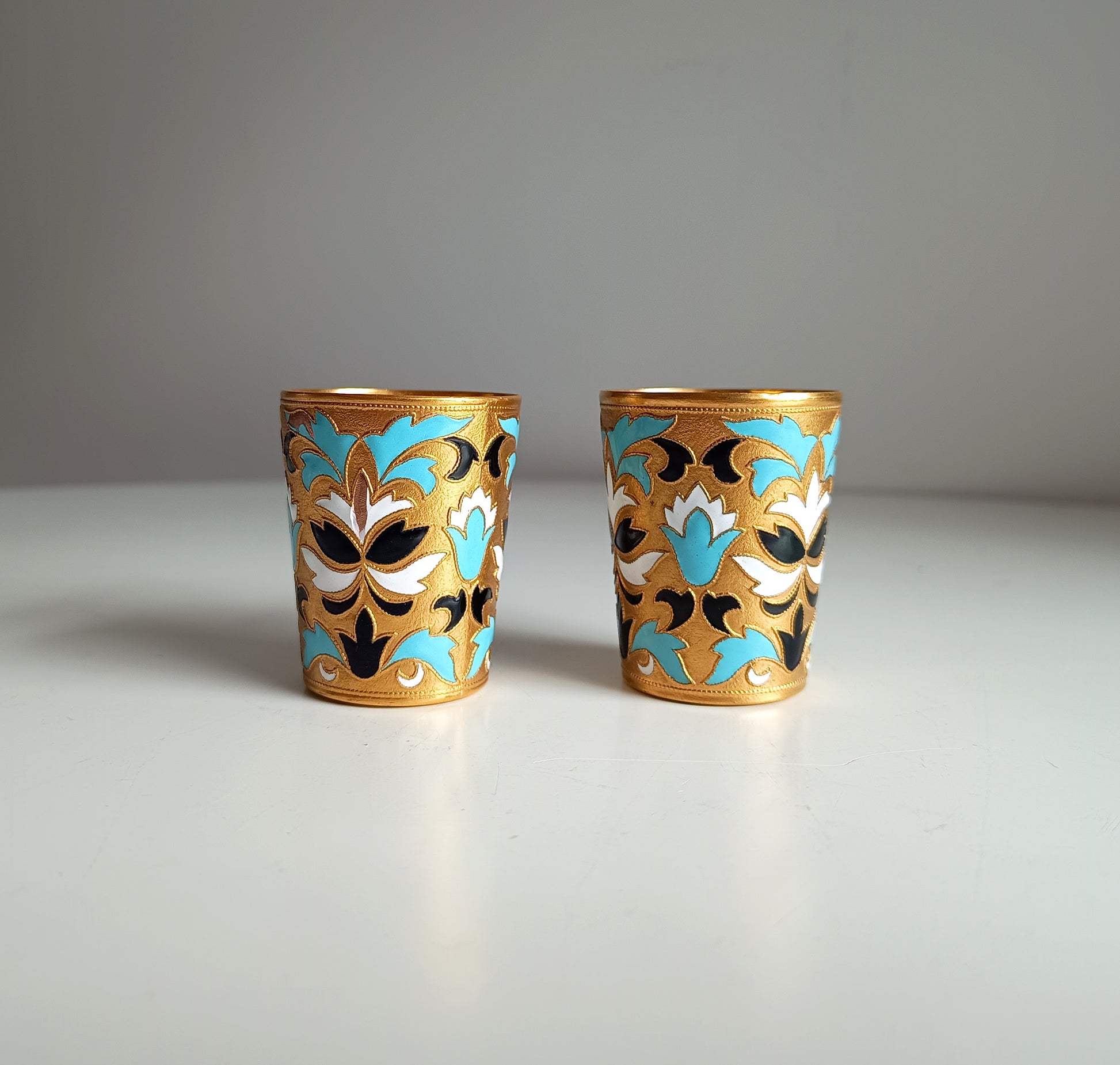Two ornate Russian enamelled blue white and gold shot glasses with floral designs