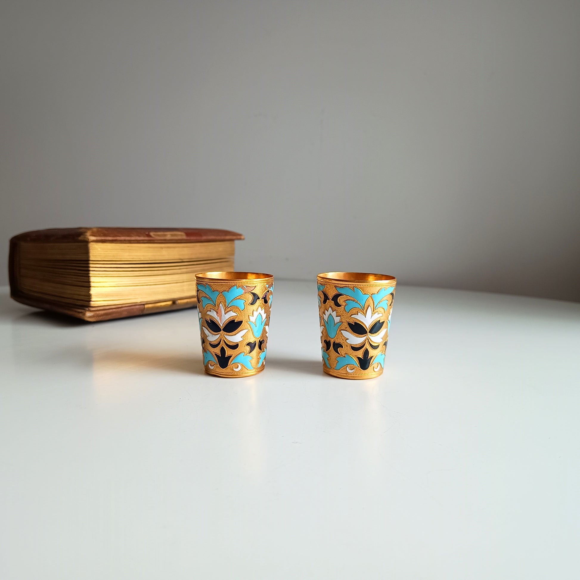 Two ornate Russian enamelled blue white and gold shot glasses with floral designs